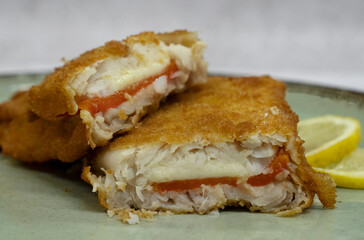 Mediterranean food. closeup view of a sliced battered hake filet stuffed with melted mozzarella cheese and red bell pepper