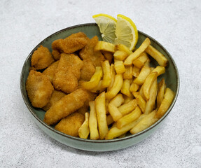 Seafood. Top view of a bowl with fried fish nuggets, lemon slices and potatoes with a white background