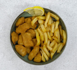 Seafood. Top view of a bowl with fried fish nuggets, lemon slices and potatoes with a white background