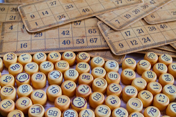 Old vintage yellowed cards and numbered tokens for playing bingo lie on an old worn surface of a table close-up, home bingo game, traditional retro board game.