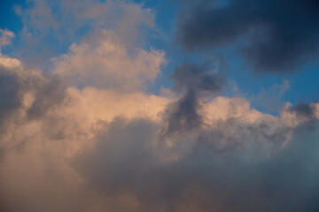 Gray-pink clouds in the blue sky illuminated by the setting sun