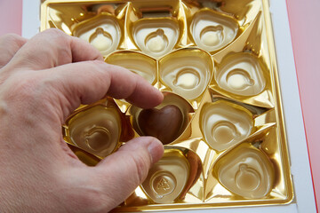 Hand taking the last heart shaped candy from a bonbonniere, Valentine's Day candy, lonely heart,...