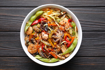 Stir-fry noodles with sea food in bowl on wooden table, top view