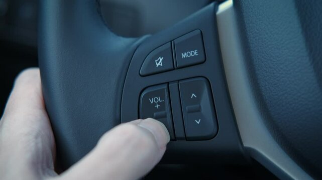 Male fingers press volume button in car. A man finger takes the music loudly during driving on road.