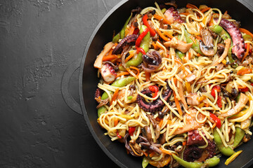 Stir-fry noodles with sea food and vegetables in wok on dark textured table, top view. Space for text