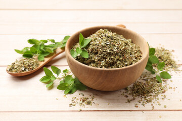 Dried oregano in bowl, spoon and green leaves on wooden table