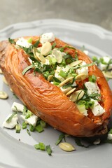 Tasty cooked sweet potato with feta cheese, pumpkin seeds and green onion on table, closeup