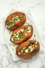 Tasty cooked sweet potatoes with feta cheese, green onion and parsley on white marble table, top view