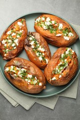 Tasty cooked sweet potatoes with feta cheese, green onion and parsley on gray textured table, top view