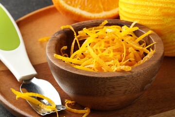 Fresh orange zest in wooden bowl and zester, closeup