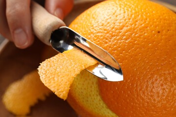 Woman zesting orange at wooden table, closeup