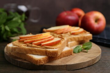 Tasty sandwiches with peanut butter, apples and mint on wooden table, closeup