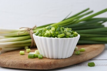 Chopped green onion in bowl and stems on white wooden table, closeup