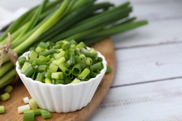 Chopped green onion in bowl and stems on white wooden table, closeup. Space for text