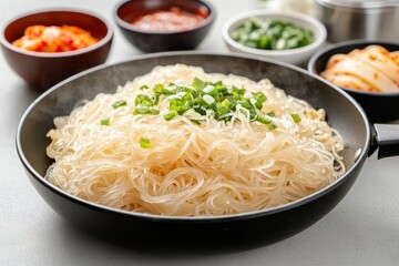 Sizzling Korean glass noodles in a skillet with vibrant condiments and side dishes on display