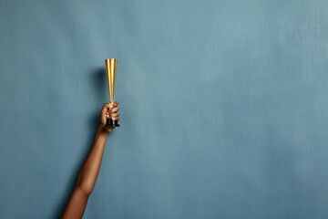Naklejka premium An African American hand triumphantly raises a mini trophy against a calming blue backdrop, symbolizing success and achievement