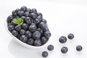 Fresh blueberries in white bowl with mint leaf on white background