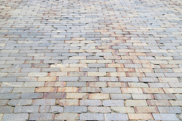 Old damaged sidewalk paved with gray and orange rectangular stone tiles with brown stains in...