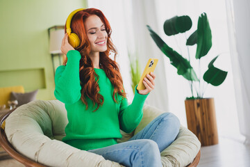 Photo of pretty young woman listen music armchair wear pullover weekend green interior apartment...