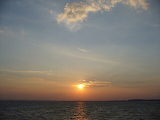 Blue sky with orange and yellow sunset over horizon of dark water surface with reflection of sunlight on water with small waves - natural evening scene. Topics: weather, natural environment, season