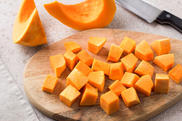 Pumpkin cut into pieces on a wooden board on a beige textured background