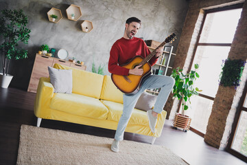 Young man enjoying a weekend at home playing guitar in a comfortable and stylish apartment with natural daylight