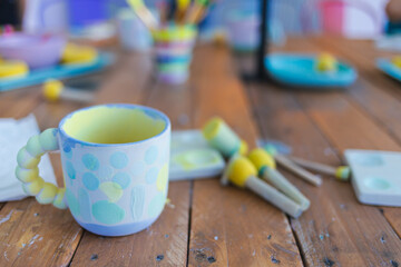 Hand painted mug on an art and craft wooden table with many tools and brushes