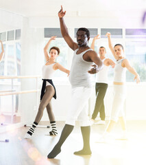 Obraz premium Motivated middle aged African American man, participating in ballet class, practicing graceful movements with group of dance enthusiasts in light-filled choreography studio..