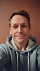 Fototapeta premium A smiling Caucasian man in a gray hoodie against a warm, muted background, exuding warmth and friendliness.