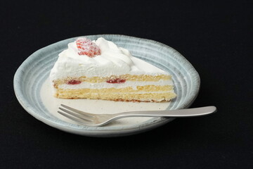 One small Japanese strawberry shortcake and a small fork on a stylish Japanese plate on a black cloth on a white table