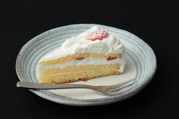One small Japanese strawberry shortcake and a small fork on a stylish Japanese plate on a black cloth on a white table