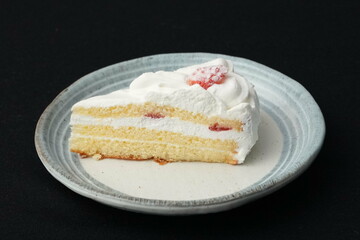 One small Japanese strawberry shortcake on a stylish Japanese plate on a black cloth on a white table