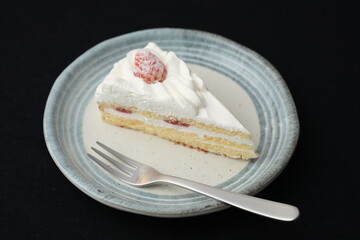 One small Japanese strawberry shortcake and a small fork on a stylish Japanese plate on a black cloth on a white table
