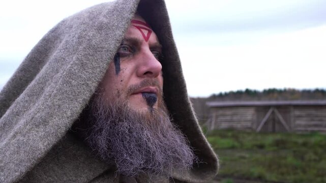 Portrait of a bearded man with face paint dressed in antique clothes hood looks away outdoor 4K