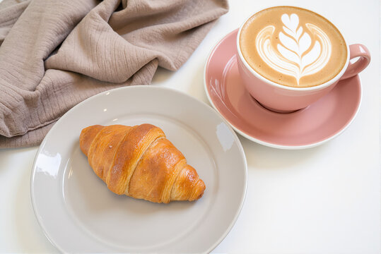 Pink cup with latte, croissant on the plate and tea towel on the white background 