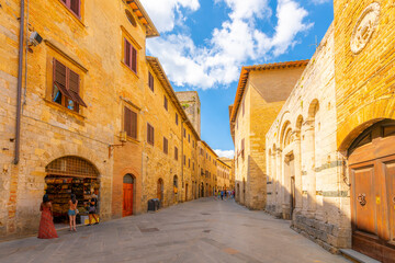 Tourists walk through a narrow stone street of cafes and shops in the historic center of the Tuscan Hill Town of San Gimignano, Italy.
