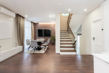 Modern Scadinavian Home Living Room. Luxurious Stylish Modern Apartment. Open Interior, TV Screen and Table with Chairs. Scandinavian Design. Flowers and Curtains. Upstairs in Background