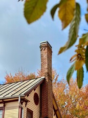 an old house with a red brick chimney in the fall on a slightly cloudy day