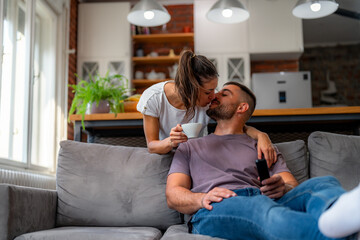 Obraz premium Woman bringing coffee to partner in living room. Man relaxing on grey sofa during morning hours, enjoying morning routine.