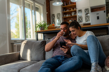 Couple relaxes on gray couch, sipping coffee and excitedly searching for their next vacation...