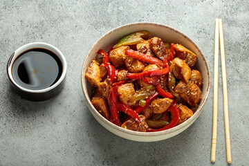 Chicken stir fry with red and green bell peppers sprinkled with sesame seeds, served in bowl, with...