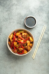 Chicken stir fry with red and green bell peppers sprinkled with sesame seeds, served in bowl, with chopsticks and soy sauce aside, composing a delicious asian meal