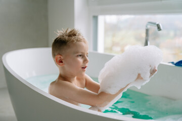 The boy enjoys a relaxing bath in the spacious bathtub with turquoise water, the spacious bathroom...