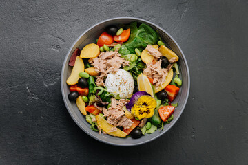 Gourmet salad bowl with tuna, poached egg, colorful vegetables, and edible flower garnish