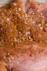 a salted piece of fresh chicken meat on paper sprinkled with spices