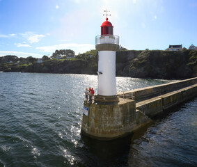 Trois personnes adultes et un enfant au pied d'un phare de Belle-Ïle-en-Mer (Le Palais) font signe à un ferry qui arrive au port © William Vallée