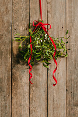 Fresh mistletoe branches with red ribbon bow hanging on wooden background