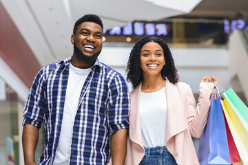 Happy african american couple walking with lost of shopping bags in department store, spending time in mall together, holding hands, free space