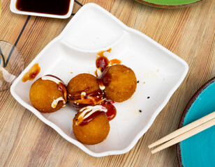 On wooden table plate with takoyaki - crispy fried dough balls containing octopus and other seafood. Popular hearty Japanese dish, restaurant menu, fast food offers.