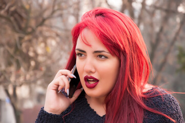 Redhead with the phone. Seductive young redhead is smiling and talking over the mobile phone in the public park